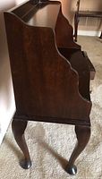 Side view showing the scalloped decorative back and cabriole leg with pad foot on the mahogany end table.