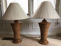 Two identical wicker table lamps with off-white fabric shades placed side by side on carpet near a window.
