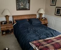 Front view of the assembled wicker sleigh queen size bed with bedding and two matching night tables each holding a lamp and items, in a bedroom.