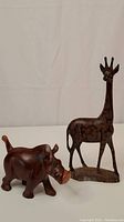 Photo showing side view of the warthog and giraffe wooden animal carvings against white background.