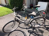 Two bicycles outdoors on a driveway in sunlight, one black and one green, showing their overall condition and color.