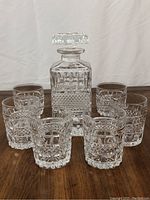 Full lot arranged with decanter in center and eight matching tumblers around it.