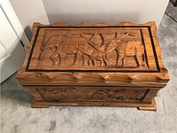 Top view of hand-carved wooden trunk showing detailed elephant carving with a tree and textured background on lid.