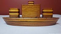 Front view of the ship-shaped wooden cribbage board showing the layered wood tones and three sections.