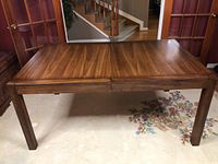 Full view of wooden dining table with leaf inserted, showing overall condition and surface.