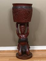 Full view of the plant stand featuring a kneeling carved figure holding a large planter above the head.