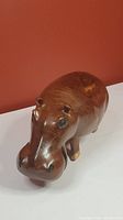 Front-side view of the brown polished wood hippo carving showing natural wood grain, carved ears, eyes, nose, and legs.