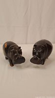 Two small to medium carved wooden hippos positioned facing forward showing front and side details. One hippo has visible wear on its left side near the rear.