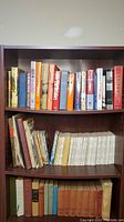 Full view of three shelves filled with vintage and newer history books and periodicals, showing a diverse range of sizes and colors.