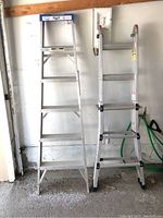 Two aluminum ladders side by side against a wall: on the left a 6-foot Lite step ladder, on the right a Vulcan multi-position ladder