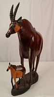 Full view of large and young antelope carvings standing on a carved wooden base