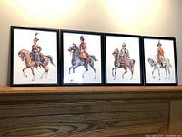 Four framed military uniform prints displayed on a wooden shelf, showing varied mounted officers in historical uniforms.