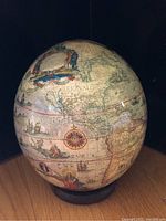 Front left angled view of ostrich egg decoupage with vintage map and compass rose, showing map section including parts of North and South America, as well as Africa.