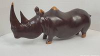 Front and side view of dark brown wooden rhino carving with natural wood color highlights on horn tip, ears, feet, and back ridge.