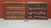 Wide view of two wooden display cases filled with multiple rows of souvenir spoons, showcasing the quantity and diversity in the collection.