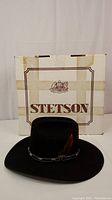 Front view of the black Stetson leather western hat with its box behind showing the Stetson logo.