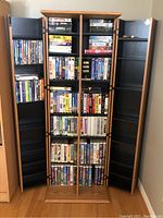 Full front view of the wooden storage cabinet filled with VHS tapes and DVDs showing the doors open revealing the items inside.