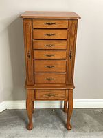 Front view of wooden jewelry box floor cabinet with six drawers and side doors closed.
