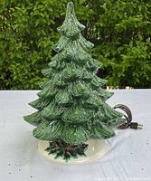 Front view of green textured ceramic Christmas tree with electrical cord, sitting on white base with painted holly details.