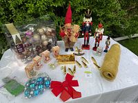 Photo showing the full lot of assorted Christmas decorations including nutcrackers, ornaments, bows, and gold garland on a table outdoors with greenery background.