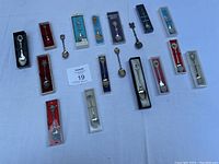 Photo of all 18 collector souvenir spoons on white surface, showing variety and mostly original packaging.
