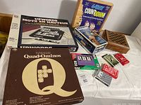 Photo showing collection of boxed board games Upwords (bilingual), Quad-Ominos, 4-Way Countdown, Boggle, Slot with multiple decks of cards on table
