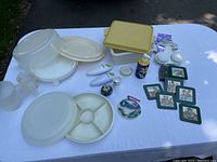 Overview of assorted kitchen items including plastic cake containers, a divided serving platter, egg poachers, and various small kitchen accessories and coasters.