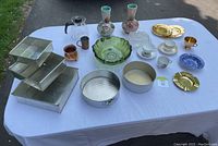 Wide shot of all kitchenware items on table including bakeware pans, vases, green glass salad bowl, assorted vintage china, metal ashtrays, and serving dishes.