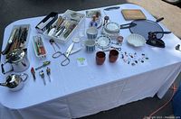 Wide view of cutlery, vintage china, kitchen tools and accessories laid out on white tablecloth