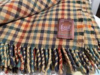 Close-up photo of Lovat brand wool blanket with plaid pattern and twisted fringed edges.