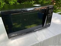 Black Panasonic microwave oven showing entire unit on a white surface outdoors.