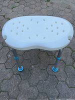 Top view of white molded plastic shower stool seat with drainage holes and kidney shape