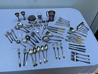 Overview of the various silver plated flatware and small tableware pieces showing tarnishing and mixture of handle styles.