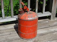 Red vintage metal gas can on a wooden surface with visible rust and paint wear.