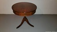 Front view of the round wooden table with three legs and a drawer closed.