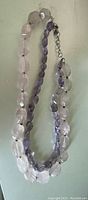 Single photo showing a double-strand necklace with rose quartz beads on one strand and amethyst beads on the other strand laid out on a flat surface.