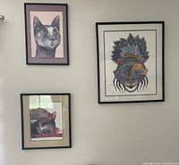 Photo showing three framed cat art prints on a wall. Two smaller prints and one larger central "Queen Cat" Mardi Gras cat print.