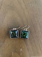 Photo of green square dangle earrings showing the green sparkle design and silver-tone metal hooks