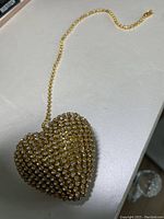 Heart-shaped gold-tone fan pull decorated with clear rhinestones and attached to a gold-tone chain, placed on a light-colored surface.