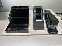 Photo of three office supply items on a white surface: desk organizer, tape dispenser, and Bostitch stapler in black plastic.