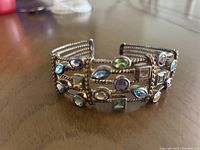 Front angle view of silver bangle with multiple faceted colored gemstones set in decorative silver frames.