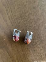 Pair of silver cloisonne earrings with multicolored enamel and detailed silver beadwork on the upper half, placed on a wooden surface.