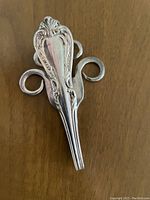 Photo of a bent silverplate fork turned into a pendant showing detailed embossed floral pattern on the handle and curled fork tines forming the shape, all polished silver.