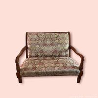 Front view of the vintage settee showing wooden arms and floral embroidery upholstery.