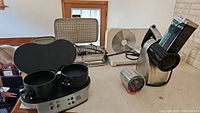 Vintage waffle iron, breakfast sandwich maker, consule electric slicer, and Cuisinart rotary grater/slicer on kitchen counter.