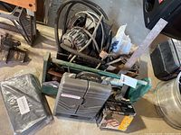 Green metal tool carrier holding various vintage automotive tools and Pontiac toolkit box, with an old motor or pump and associated tubing behind it.