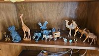Wide shelf view showing assortment of carved animal figurines including wood giraffe, dog, camels, horse and buggy, soapstone seal, bunnies, loon and glass deer with babies