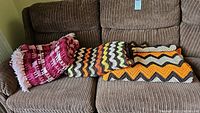 Three vintage handmade crochet blankets folded on a couch, showing various colors and patterns.