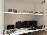 Shelf with multiple eyeglasses and eyeglass cases arranged showing variety of styles and cases included.