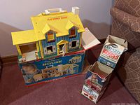 Fisher Price Play Family House displayed with its original box and two boxes of Easy-lock bricks next to it on a carpeted floor.